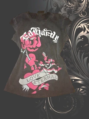 Svart Ed Hardy t-shirt med tryck - Cool svart t-shirt från Ed Hardy med stort grafiskt tryck i rosa och vitt framtill. Motivet har rosor, hjärta och texten 'Love Eternal'. T-shirten har korta ärmar och en figurnära passform. Perfekt för dig som gillar statement-plagg och streetstyle.
