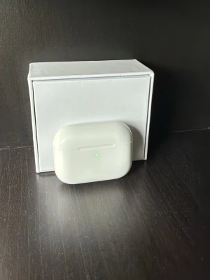 AirPod Pro 3 - Snygga vita trådlösa in-ear hörlurar med laddningsetui. Hörlurarna har en stilren och kompakt design med mjuka silikonproppar och laddningsindikator på framsidan av etuiet. Perfekta för musik, poddar och samtal på språng.