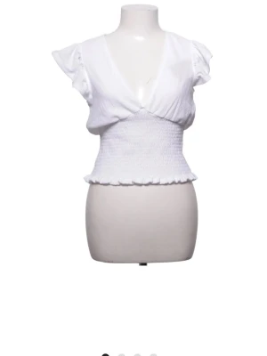 Vit topp från  Gina Tricot - Söt vit topp från Gina Tricot med omlottdesign och v-ringning. Toppen har korta volangärmar och smockad midja som ger en snygg passform. Perfekt till sommaren och lätt att matcha med olika stilar, köptes på sellpy men passade inte riktigt mig💕