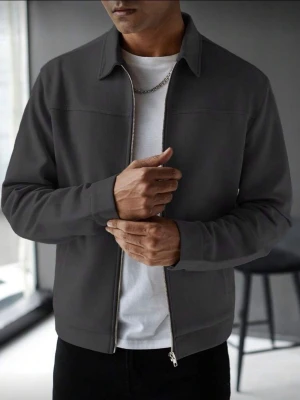 Mörkgrå overshirt med dragkedja - Stilren mörkgrå overshirt med rak passform och klassisk krage. Jackan har hel dragkedja framtill och diskreta sidofickor. Tillverkad i ett mjukt, slätt material som ger en clean look. Perfekt att bära över en t-shirt för en avslappnad men snygg stil.