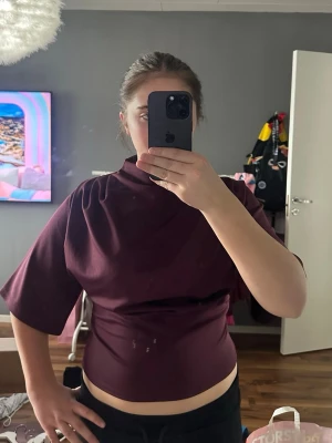 Vinröd topp med halvpolo - Säljer en vinröd topp med halvpolo och korta, vida ärmar. Toppen har en slim passform ochä materielet är inte så stretchigt utan mer fast. Perfekt för dig som gillar stilrena plagg med en twist.