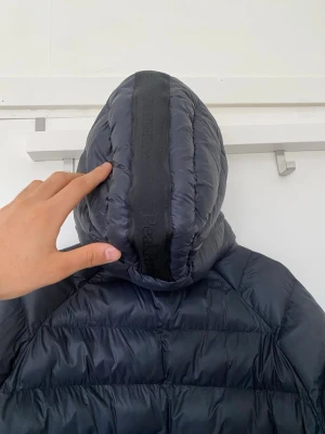 Svart dunjacka Peak Performance - Snygg svart dunjacka från Peak Performance med huva och dragkedja framtill. Jackan har ribbade muddar vid ärmsluten och diskret logga på bröstet. Perfekt för kalla vinterdagar tack vare det värmande dunmaterialet. Pris kan diskuteras 