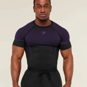Gymshark svart/lila seamless t-shirt onyx v5 - Säljer en tight seamless t-shirt från Gymshark i svart med lila detaljer. T-shirten har korta ärmar och är tillverkad i ett stretchigt syntetmaterial som passar perfekt för träning. Snygg sportig design med diskret logga på bröstet.