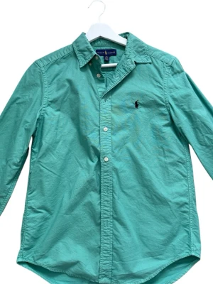 Grön skjorta från Ralph Lauren - Klassisk grön skjorta från Ralph Lauren med lång ärm och knappar framtill. Skjortan har en broderad logga på bröstet och är tillverkad i bomull. Passar runt 165/175cm lång, pris kan diskuteras, hör av er vid fler frågor.