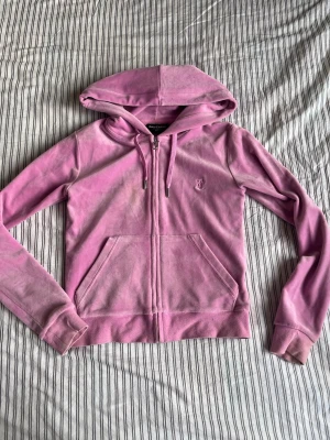 Rosa velourhoodie från Juicy Couture - Säljer en överdel från Juicy Couture med dragkedja, huva och fickor. Klassisk logga broderad på bröstet och ribbade muddar. 