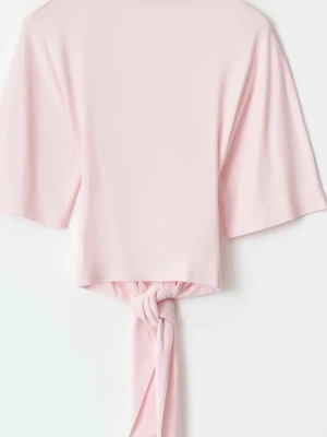 Ljusrosa topp med  rosett på ryggen - Supersöt ljusrosa topp med rosett/knut på ryggen och halvlånga ärmar. Toppen är croppad och har en mjuk, stretchig känsla som gör den bekväm att bära. Perfekt att styla med låga jeans eller kjol för en trendig look.