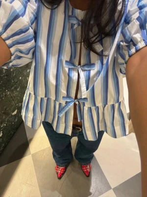 Ganni Cotton Poplin Peplum Blouse, striped - GANNI COTTON POPLIN PEPLUM BLOUSE  Blus från Ganni. Cotton Poplin Peplum Blouse är tillverkad av 100% ekologisk bomull och är designad med en avslappnad passform. Toppen är försedd med en rund halsringning med knytning och puffärmar.  Använd 2 gånger. Inget att anmärka på.