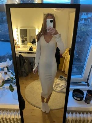 Beige ribbad långklänning med v-ringning - Säljer en stilren beige långklänning med v-ringad hals och långa ärmar. Klänningen är ribbad och har en kroppsnära passform som framhäver siluetten. Perfekt för dig som gillar minimalistisk och elegant stil. Slits på ärmarna!