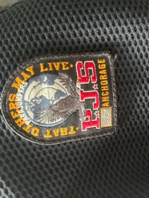 Svart jacka från Parajumpers - Snygg svart cardigan från Parajumpers med coolt patch på axeln och orange detalj. Jackan har meshfoder och är perfekt för kyligare dagar. Modellen heter Warm Up och har en sportig look. Den har nu blivit för liten. Passar dig som är 164-170 cm lång. Storleken är Youth large. Pris ej hugget i sten, hör av er vid funderingar!