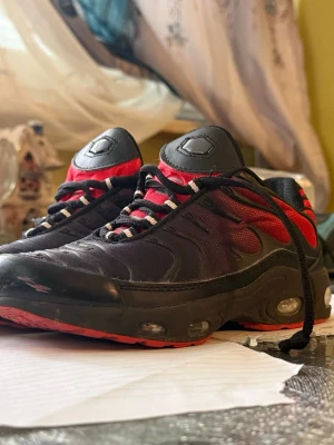 Svarta och röda sneakers med luftdämpning - Snygga sneakers i svart och rött med coola detaljer och luftdämpad sula. Skorna har svarta och vita snören, meshpaneler för extra ventilation och en sportig look. Perfekta för dig som gillar streetwear och vill sticka ut med din stil.