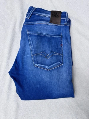 Blå jeans från Replay - Snygga blå slim fit jeans från Replay med klassisk femficksdesign och lätt slitna detaljer på låren. Jeansen har normal midja, dragkedjegylf och är tillverkade i ett mjukt denimtyg som ger en bekväm passform. !!det finns ett litet hål vid gylfen!! 