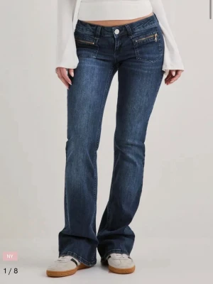 Mörkblå bootcut jeans med dragkedjor  - Snygga mörkblå bootcut jeans från Nelly med dekorativa dragkedjor framtill och klassiska bakfickor. Jeansen har låg midja och är tillverkade i stretchigt denim för en bekväm passform. Perfekta för en trendig och avslappnad stil. Använda en gång