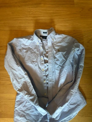 Ljusblå skjorta från Ralph Lauren - Klassisk ljusblå skjorta från Ralph Lauren med broderad logga på bröstet. Skjortan har knappar framtill och på kragen samt lång ärm. Perfekt för en clean och stilren look.