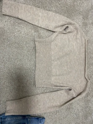 Beige stickad tröja med ribbad kant - Säljer en beige stickad tröja med långa ärmar och bred ribbad kant i midjan och vid ärmsluten. Tröjan har en enkel, stilren design och är perfekt för lager på lager. Passar till både jeans och kjol.