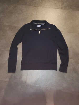 Mörkblå ziptröja från Jack & Jones - Snygg mörkblå tröja från Jack & Jones med halv dragkedja framtill och hög krage. Tröjan har långa ärmar och ribbade muddar vid ärmslut och nederkant. Perfekt för en stilren och avslappnad look.