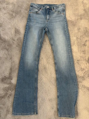 Ljusblå jeans kappahl - Snygga ljusblå bootcut jeans från Kappahl med högmidja. Jeansen har en lätt tvättad look och är tillverkade i mjuk denim med knapp och dragkedja framtill. Perfekta för en avslappnad och trendig stil. Använda 2 gånger 