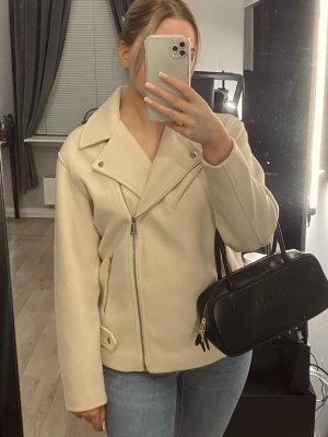 Beige kappa - Snygg beige kappa med bred krage och dragkedja framtill. Kappan har fickor med dragkedja och en stilren, rak passform.