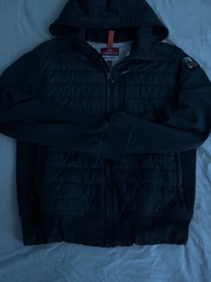 Svart fleecejacka från Parajumpers - Svart fleecejacka från Parajumpers med luva och quiltad framsida. Jackan har dragkedja och en patch på ärmen. Perfekt för kyliga dagar och har en sportig look.