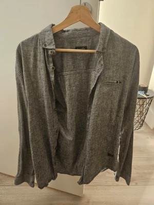 NY grå skjorta  - Säljer en ny grå skjorta, aldrig använd, bara etiketten är borttagen i mjukt bomullsmaterial. Skjortan har knappar längs bröstet, en liten bröstficka med dragkedja och avslappnad passform. Storleken på etiketten är XL, men enligt min mening passar den bättre för storlek L.