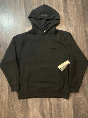 Essentials Svart – Helt ny - Helt ny svart Essentials hoodie. Aldrig använd och i perfekt skick.  Svart färg är alltid mest eftertraktad och lätt att matcha. Riktig clean streetwear vibe.  • Skick: 10/10 • Klassisk svart • Säljs snabbt vid rätt bud