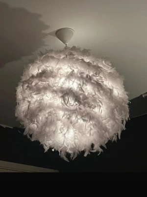 Vit fjäderlampa taklampa rund - Säljer en rund taklampa med vita fjädrar som ger ett mjukt och fluffigt intryck. Lampan sprider ett behagligt ljus och blir en snygg inredningsdetalj i rummet. Passar perfekt för dig som vill ha något unikt i taket.