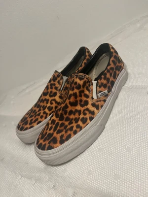 Vans slip-on leopardmönstrade sneakers - Leopardmönstrade slip-on sneakers från Vans med vit sula och svart innerfoder. Skorna har en klassisk låg siluett och är tillverkade i canvasmaterial. Perfekta för dig som vill sticka ut med ett djuriskt mönster och enkel design. OBS!! Storlek Men US 6 / Women US 7,5 . Använda en gång.
