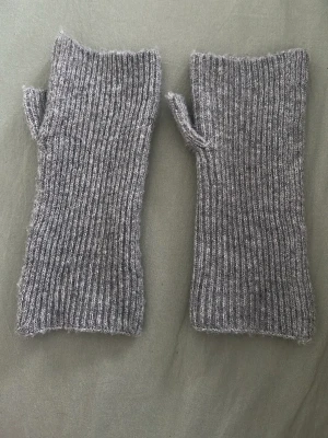 Grå stickade torgvantar - Säljer ett par grå stickade torgvantar i mjukt garn. Vantarna är ribbstickade och har öppna fingrar samt tumme, perfekta för dig som vill hålla händerna varma men ändå kunna använda mobilen. Klassisk och enkel design.