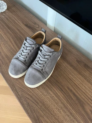 Grå mockasneakers med röd sula - Snygga grå sneakers i mocka med vita sulor och cool röd detalj undertill. Klassisk låg modell med snörning och diskret design som passar till det mesta. Skön innersula och stilren look.