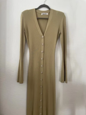 Beige ribbad långklänning Adoore - Supersnygg beige långklänning från Adoore med ribbad struktur och v-ringning. Klänningen har långa ärmar, knappar hela vägen framtill och en figurnära passform. Perfekt för dig som gillar stilrena och trendiga plagg. Orginalpris: 1595kr