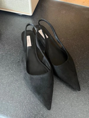 Svarta spetsiga klackskor  - Säljer ett par snygga svarta klackskor med spetsig tå och öppen häl med smal rem. Klackhöjden är 4 cm. De har inte används utomhus utan bara testats💞