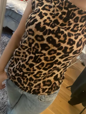 Leopardmönstrad topp med kort ärm - Snygg topp med leopardmönster i bruna och svarta toner. Modellen har korta ärmar och en avslappnad passform. Perfekt för dig som vill sticka ut med ett djurmönstrat plagg. Tyget känns mjukt och följsamt.