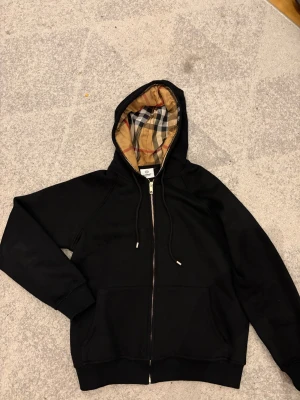 Burberry zip hoodie - Tja! Säljer nu en svart burberry hoodie i storlek S-Xs. Tröjan har en klassisk rutig luva i beige, svart och rött. Tvivla inte på att höra av er vid minsta fundering! Ha det fint!