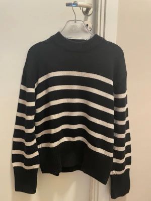 Svartvit randig stickad tröja Gina Tricot - Säljer en svart stickad tröja från Gina Tricot med vita horisontella ränder. Tröjan har rund hals, långa ärmar och ribbade muddar vid ärmslut och nederkant. Perfekt för dig som gillar en klassisk och avslappnad stil.