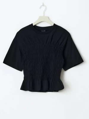 Svart smockad topp - Trendig svart topp med smockad midja och volangkant nedtill. T-shirten har rund halsringning och korta ärmar, vilket ger en snygg och bekväm passform. Perfekt att styla med jeans eller kjol för en cool look.