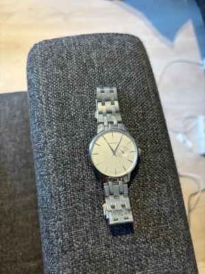 Silverfärgad Gant klocka i metall - Klassisk klocka från Gant i silverfärgad metall med stilren länkarmband. Urtavlan är enkel och ljus med minimalistiska markeringar och en liten sekundvisare. Perfekt för dig som gillar en clean och tidlös accessoar.