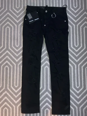 Svarta distressed jeans från Dsquared2 - Säljer ett par svarta Dsquared2 New Rider Jean i storlek 36. Helt nya och oanvända med samtliga originaltaggar kvar. Modellen har stilrena slitningar framtill och snygga detaljer som ger en modern och exklusiv look. Perfekta både till vardag och mer uppklädda tillfällen. Jeansen är i toppskick och nypris är betydligt högre. Ett bra tillfälle att köpa äkta designer till ett bättre pris. Först till kvarn gäller. Hör av dig vid intresse. Priset kan diskuteras. Perfekta för en edgy och trendig stil.
