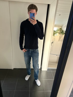 Carmes cashmere hoodie  - En stilren mörkblå hoodie med huva och dragsnören. Hoodien har en klassisk passform och är tillverkad i ett mjukt material som känns skönt mot huden. Perfekt för dig som gillar en enkel och clean look.