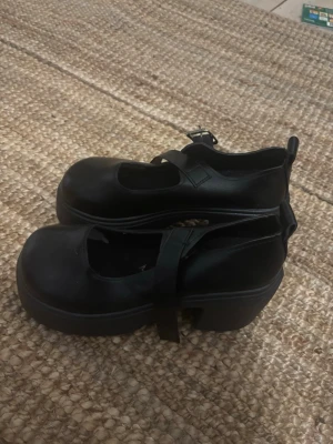 Svarta Mary Jane ballerinaskor - Säljer ett par svarta Mary Jane ballerinaskor med chunky platåsula och justerbart spänne över foten. Skorna har rund tå och är tillverkade i ett slätt material som ger en stilren look. Perfekta för dig som gillar en edgy men klassisk stil. dom är 41 men funkar om man har storlek 40 dom funkade för mig iallafall 