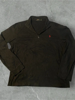 Svart halvzip från Polo Ralph Lauren | L - Säljer en svart långärmad halvzip-tröja från Polo Ralph Lauren. Tröjan har en klassisk krage med dragkedja och den ikoniska röda logotypen broderad på bröstet. Perfekt för en stilren och avslappnad look.