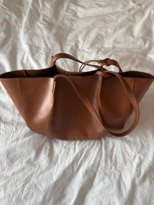 Brun väska  - Fin brun väska som man får plats med mycket i.  Höjd: 24.5 cm i storlek One Size Längd: 42 cm i storlek One Size Vidd: 14 cm i storlek One Size