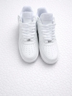 Helvita Nike Air Force 1 sneakers - Klassiska helvita Nike Air Force 1 sneakers med låg profil. Skorna har en chunky sula, perforerade detaljer på tån och Nike-logga på plösen. På Tillverkade i slätt läder för en clean och tidlös look.