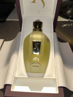 Xerjoff Naxos parfym, inte ens sprayats 10 gånger har kvitto - Exklusiv parfym från Xerjoff, modellen Naxos. Flaskan är elegant med guldfärgad kork och detaljer, och levereras i en lyxig lila box med guldfärgade inslag. Flaskan har en mjuk, rundad form och tydlig logotyp framtill.