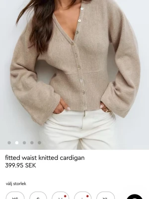 Beige ribbad kofta med v-ringning - Trendig beige kofta med v-ringning och breda ärmar. Koftan har ribbad midja som ger en snygg siluett och stängs med silvriga knappar framtill. Stickad i mjukt material, perfekt för lager på lager och en clean look.