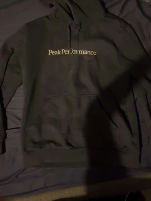 Mörk blå hoodie från Peak Performance - Säljer en mörk blå hoodie från Peak Performance med vit logga tryckt på bröstet. Hoodien har klassisk känguruficka framtill och justerbar dragsko i huvan. Perfekt för dig som gillar stilrena och bekväma plagg.