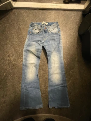 Ljusblå bootcut jeans med slitningar stlk 134/146 - Säljer ett par ljusblå bootcut jeans med snygga slitningar och utsvängda ben. Jeansen har klassiska fem fickor och coola detaljer på bakfickorna. Perfekta för en avslappnad och trendig look, dragkedja i gylfen.  Stlk svårt att se på lappen men jag TROR stlk 9-10 år. Innerbenslängd 65 cm Ytterlängd 85 cm