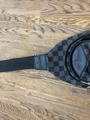 Louis Vuitton axelväska Damier Graphite - Snygg axelväska från Louis Vuitton i det klassiska Damier Graphite-mönstret. Väskan är svart och grå med justerbar axelrem i textil och detaljer i läder. Praktisk dragkedja och flera metalldetaljer. Perfekt för dig som vill ha en trendig och exklusiv accessoar.