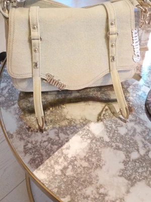 Ljusblå denimväska från Juicy Couture - Säljer en ljusblå axelremsväska i denim från Juicy Couture. Väskan har silverfärgade detaljer, dekorativa spännen och Juicy-logga i strass framtill. Perfekt för dig som gillar en trendig och avslappnad stil.lite smuts av foundation finns kolla någa bild 2