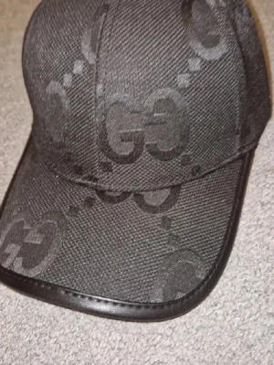 Svart GG-keps från Gucci - Snygg svart keps från Gucci med GG-monogram i ton-i-ton över hela kepsen. Kepsen har böjd skärm med läderkant och är tillverkad i ett slitstarkt tygmaterial. Perfekt för dig som gillar exklusiva accessoarer med streetwear-vibe.