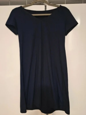 Mörkblå kortärmad klänning - En enkel och stilren mörkblå klänning med korta ärmar och v-ringad hals. Klänningen har en rak passform och är perfekt för dig som gillar minimalistisk stil. Passar till många olika tillfällen och är lätt att matcha med accessoarer.