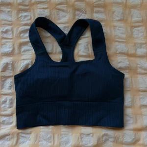 Mörkblå sport-bh från TRIDRI - Säljer en mörkblå sport-bh från TRIDRI med breda axelband och brottarrygg. Bh:n är ribbad i materialet och har en stilren, sportig design med uttagbar vaddering🦋